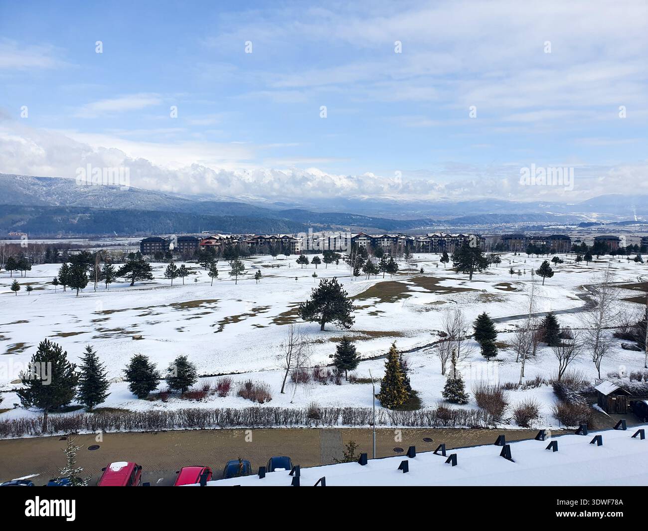 Schneebedeckter Golfplatz und offene Felder mit immergrünen Bäumen, eingerahmt von entfernten Resortgebäuden und sanften Bergen unter einem hellblauen Himmel Stockfoto