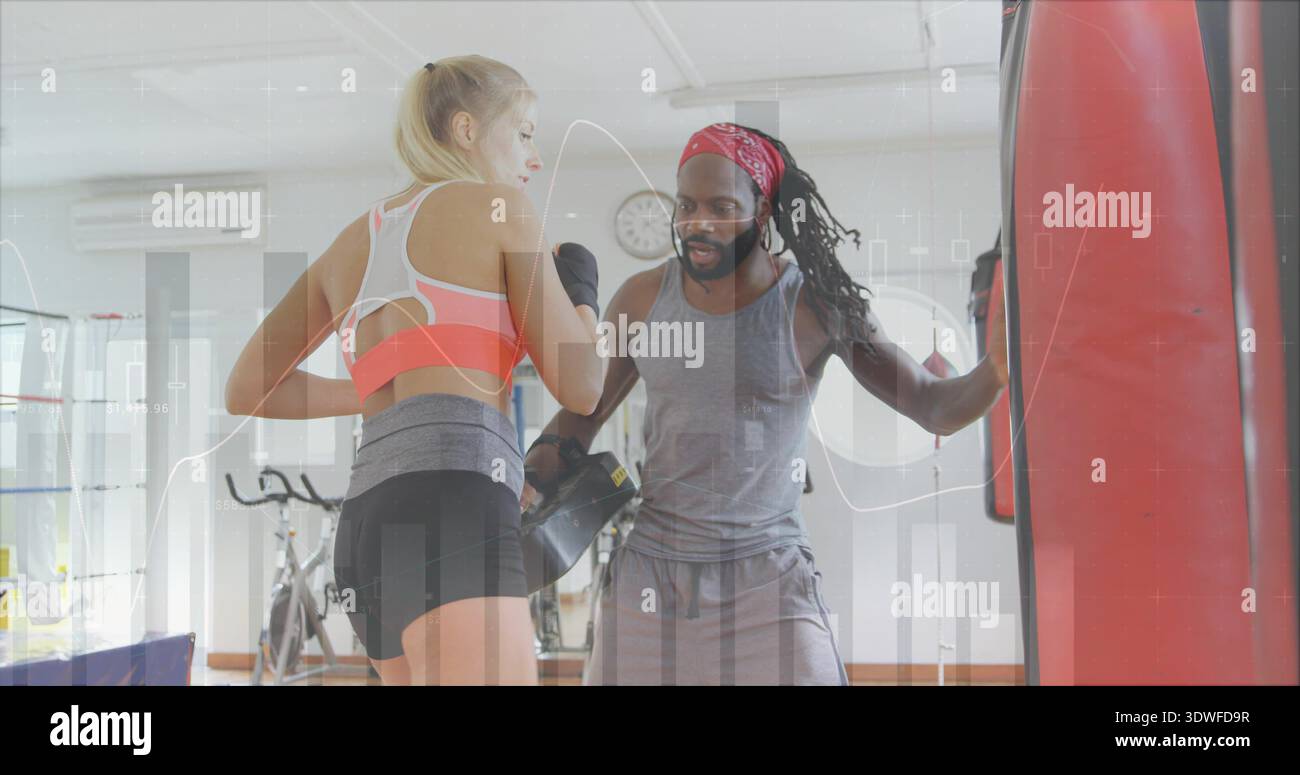 Der Trainee mit rosa-grauen Sport-BHs und schwarzen Shorts im Fitnessstudio, der Trainer hält Focus-Handschuhe Stockfoto