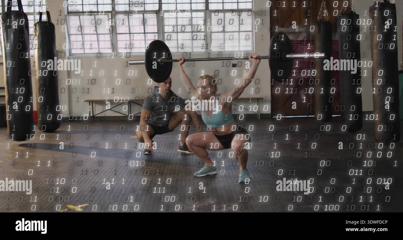 Eine Frau in blauem BH hebt die Langhantel im Fitnessstudio an, der Trainer sieht sie unter einem Binärüberzug Stockfoto
