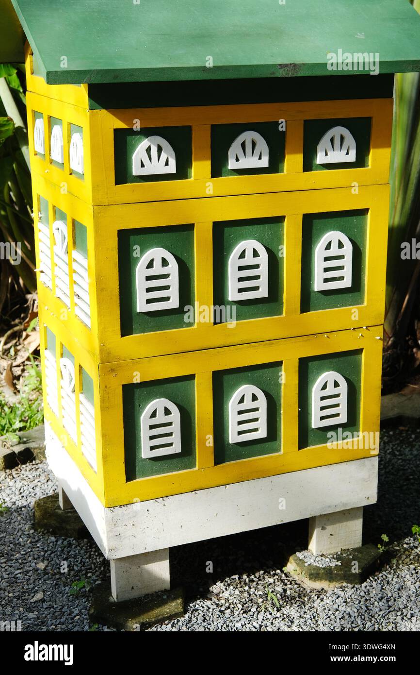 Farbenfrohes Bienenstockmodell, das einem Märchenhaus ähnelt, mit gelben und grünen Farben, dekorativen Fenstern und einem abgeschrägten Dach in einem Gartenbereich Stockfoto