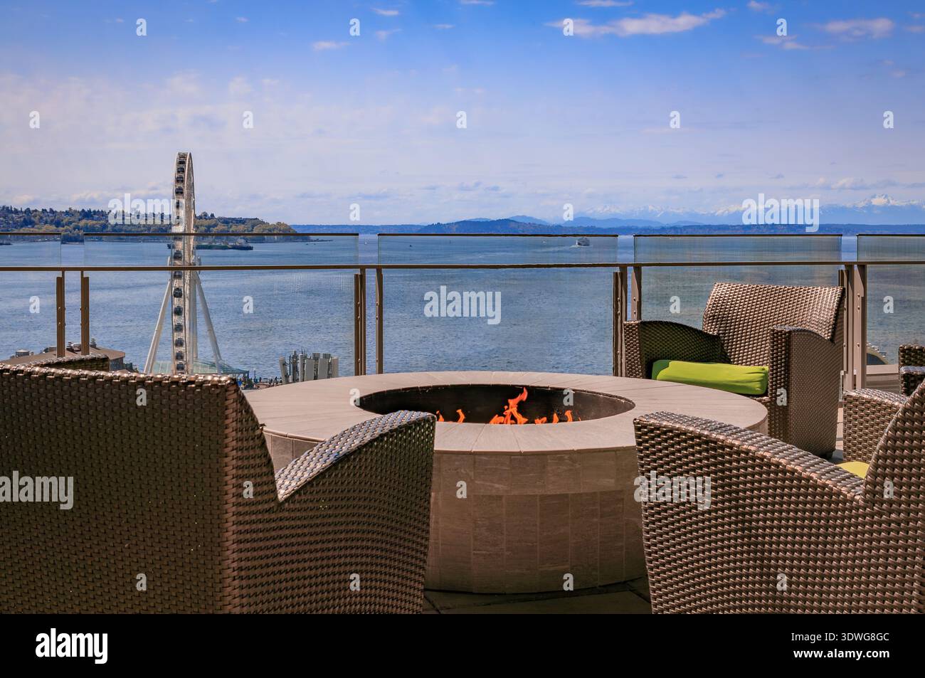 Korbsessel umgeben eine runde Steinfeuerstelle in einer Dachlounge mit Blick auf das Great Wheel, den Puget Sound und die Olympic Mountains in Seattle, USA Stockfoto