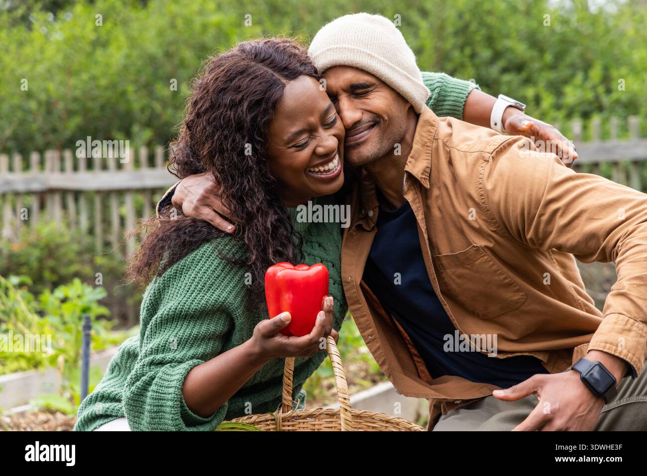 Verschiedene Pärchen sitzen im Garten, lachen, während sie roten Pfeffer halten, Frau in Pullover Stockfoto