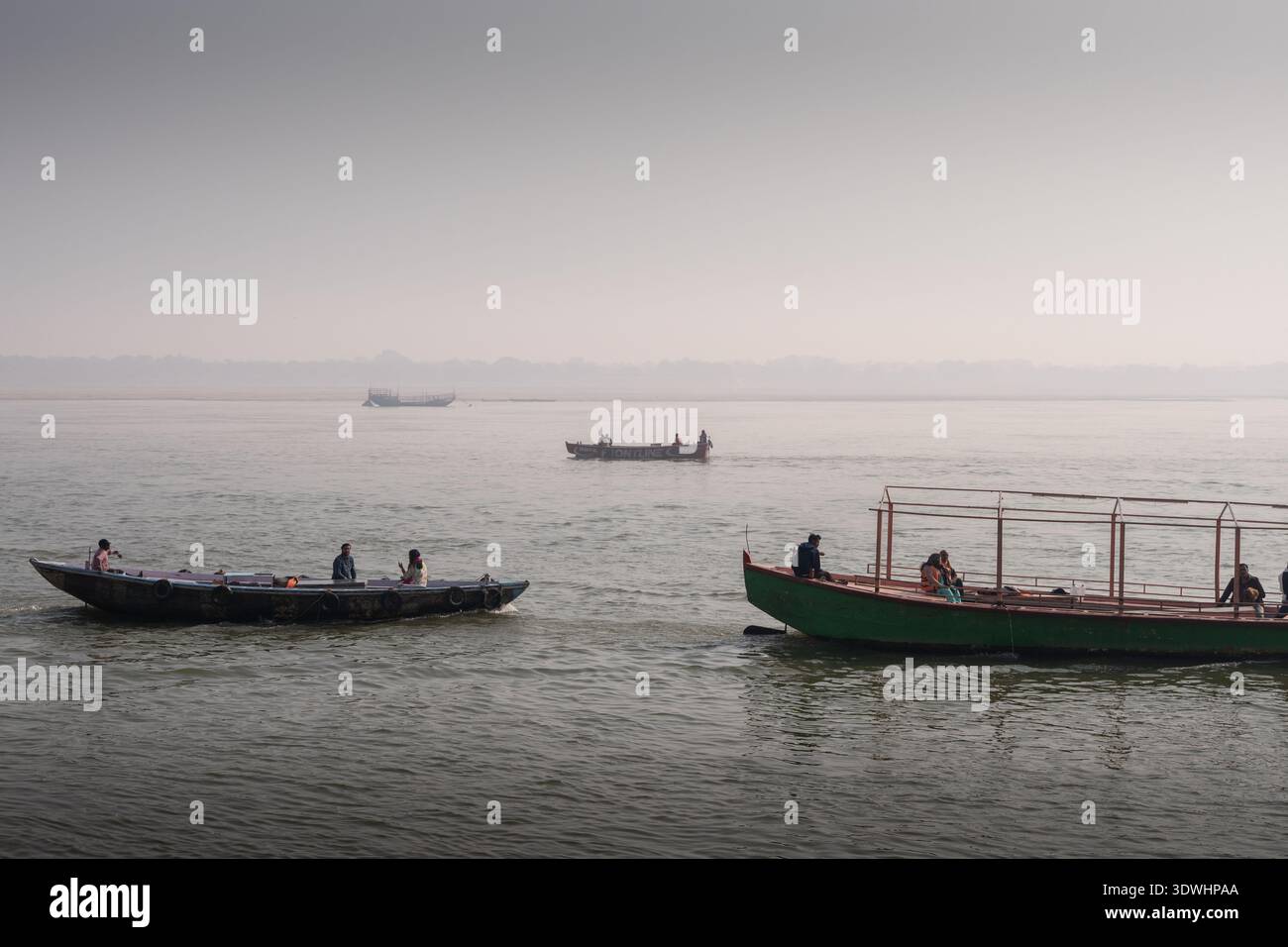 Mehrere Boote mit Menschen auf dem Ganges in Varanasi, Indien, unter einem trüben Himmel. Stockfoto