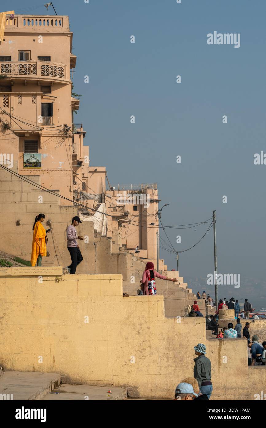 Die Menschen genießen die Stufen und Ghats am Fluss in Varanasi, Indien, mit historischen Gebäuden im Hintergrund. Stockfoto