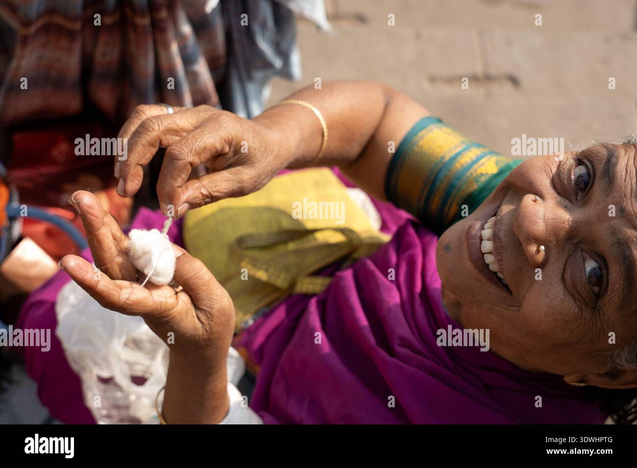 Lächelnde ältere indische Frau in farbenfrohem Sari, die Baumwolle in den Händen hält in Varanasi, Indien. Stockfoto
