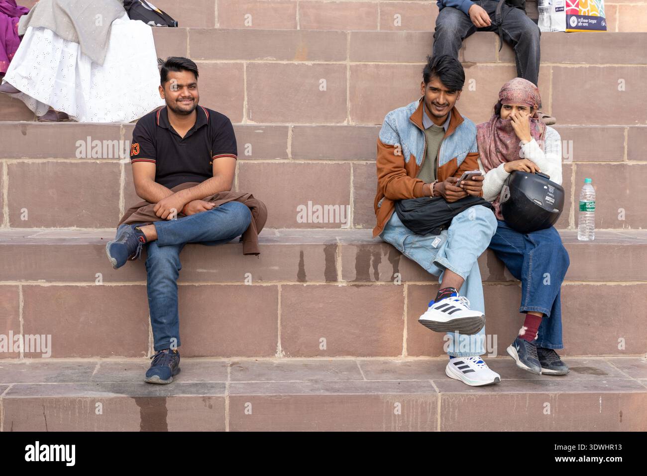 Drei junge Erwachsene sitzen auf Steintreppen in Varanasi, Indien, und genießen einen ungezwungenen Moment im Freien. Stockfoto