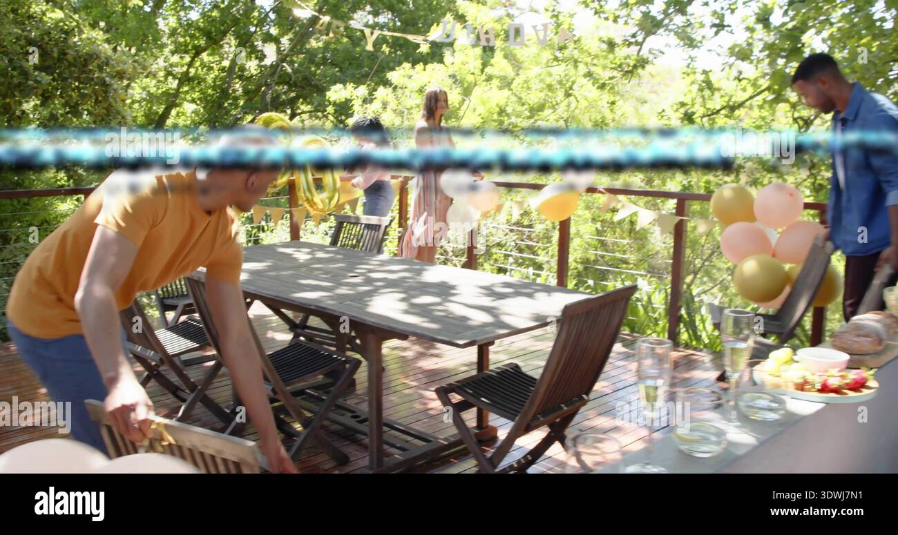 Arrangieren Sie zwanglose Gastgeber, die Klappstühle um einen Holztisch auf Deck mit pinkfarbenen Ballons bewegen Stockfoto