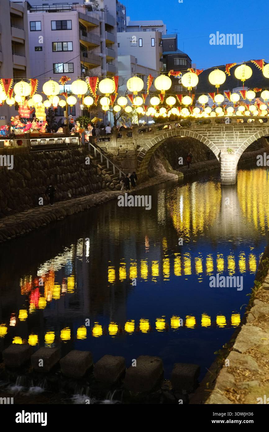 Beleuchtete gelbe Laternen spiegeln sich im Nakashima River von der historischen Meganebashi Spectacles Bridge bei Nacht, Nagasaki Stockfoto