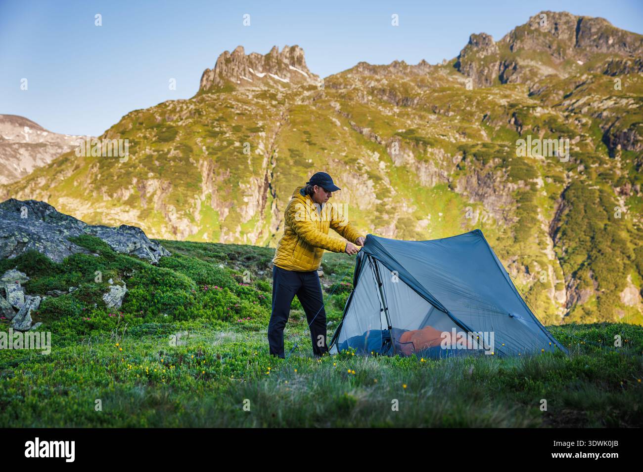 Wanderer, der Zelt in den Bergen aufstellt. Mann, der während des Trekking-Trips ein ultraleichtes Zelt aufbaut. Outdoor-Survival und alpines Lifestyle-Konzept Stockfoto