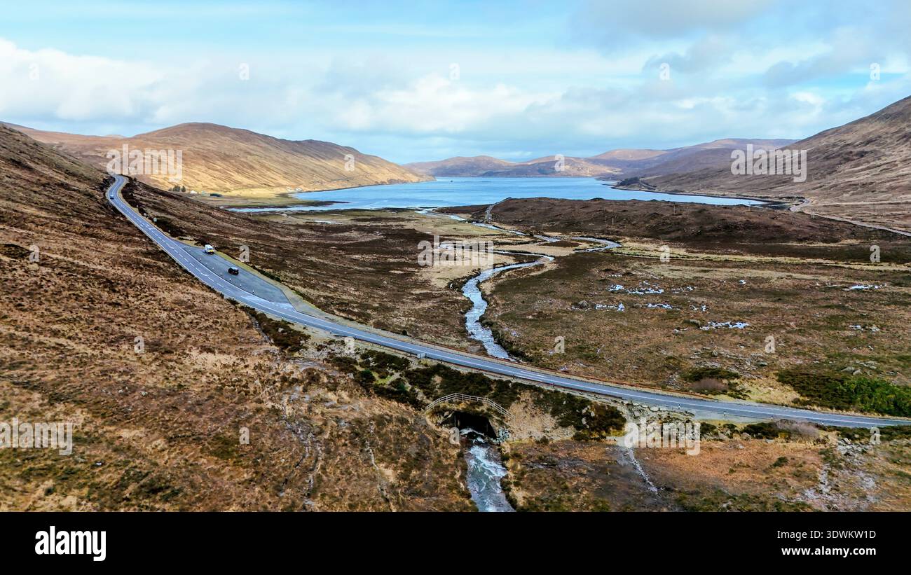 Schlängeln Sie sich durch die wilde Schönheit der schottischen Highlands, wo die Straße auf endlosen Himmel trifft und ein ruhiges Loch die Seele der Natur reflektiert Stockfoto