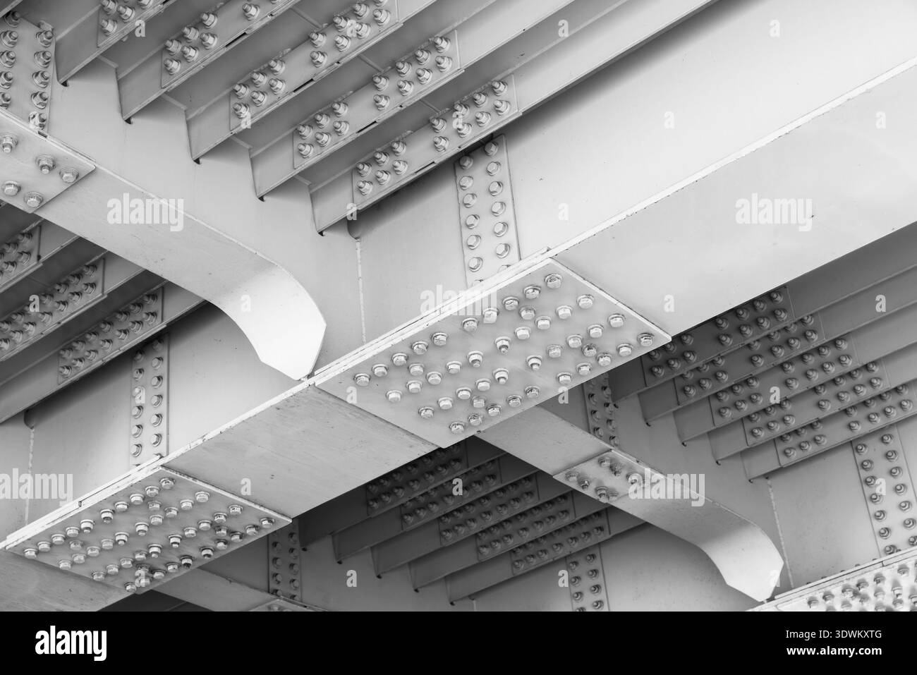 Nahaufnahme der Unterseite einer weiß lackierten Stahlbrücke mit genieteten Trägern, sich wiederholenden Rippen und strukturellen Spannweiten. Ideal für Architekturen Stockfoto