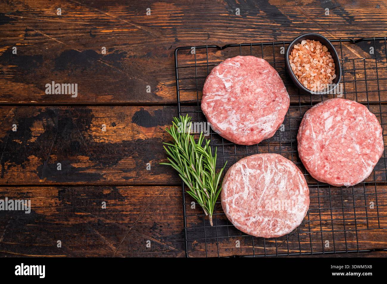 Gefrorene Fleischpasteten, bereit zum Grillen, Forcemeat von Schwein und Rindfleisch für Burger. Hölzerner Hintergrund. Draufsicht. Stockfoto