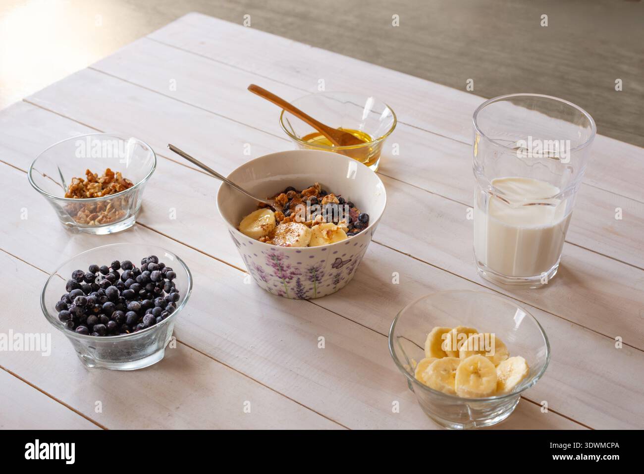 Nahrhafte Porridge Schüssel mit Banane, gefrorenen Heidelbeeren und Walnüssen serviert mit Milch und Honig, gesundes Frühstückskonzept Stockfoto