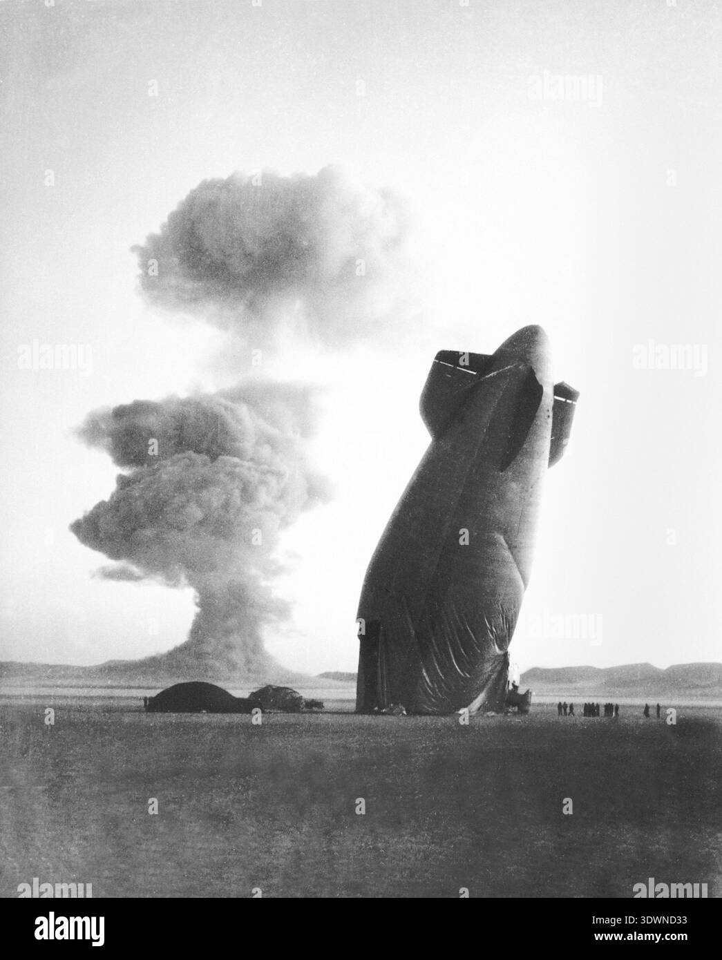 Dieses beeindruckende Foto aus dem Jahr 1957 zeigt die dramatische Szene am Nevada Test Site, wo der Heckteil eines Goodyear ZSG-3-Blitzes der US Navy vor der bedrohlichen „Stokes-Wolke“ steht, die durch eine nukleare Detonation im Hintergrund gebildet wurde. Das Bild veranschaulicht eindrucksvoll die Ängste des Kalten Krieges der Ära und die krasse Realität der Atomtests. Stockfoto