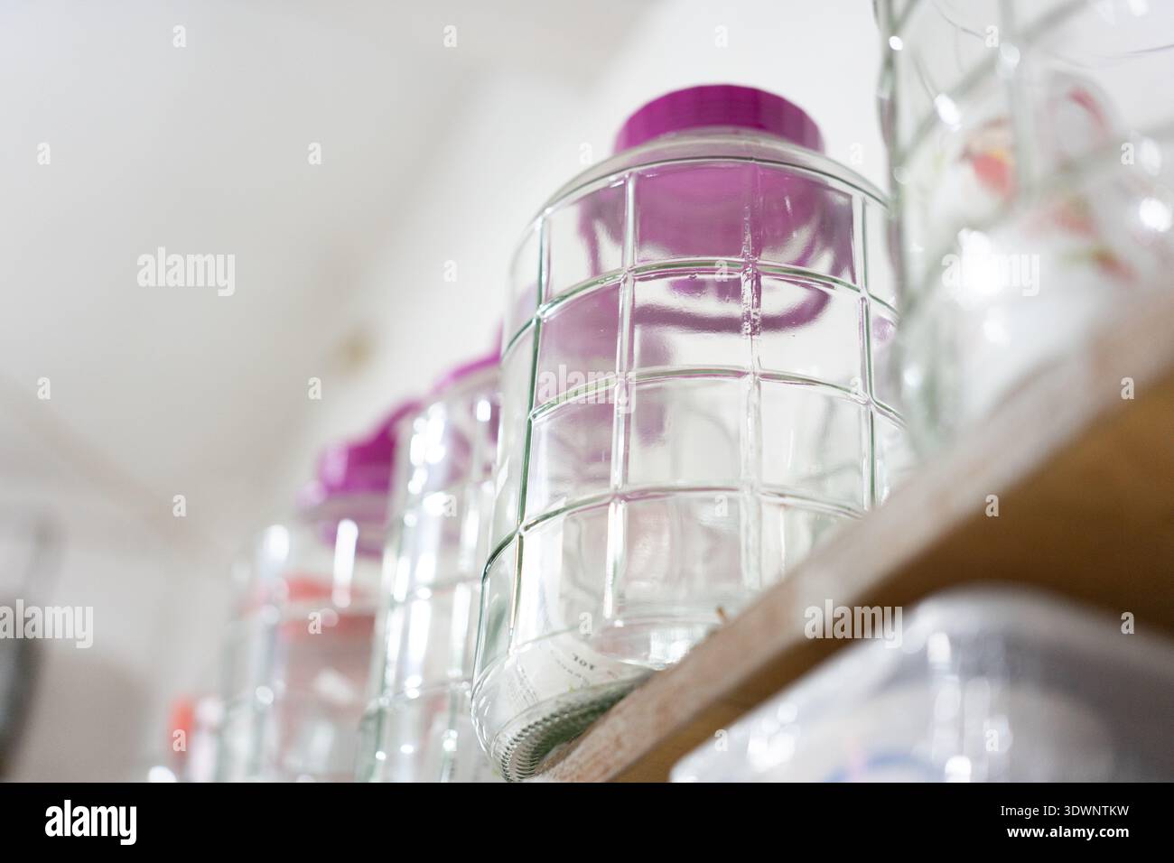 Glasgläser mit lila Deckeln auf Holzregal in der Küchenaufbewahrung, saubere und organisierte Hausküche Stockfoto