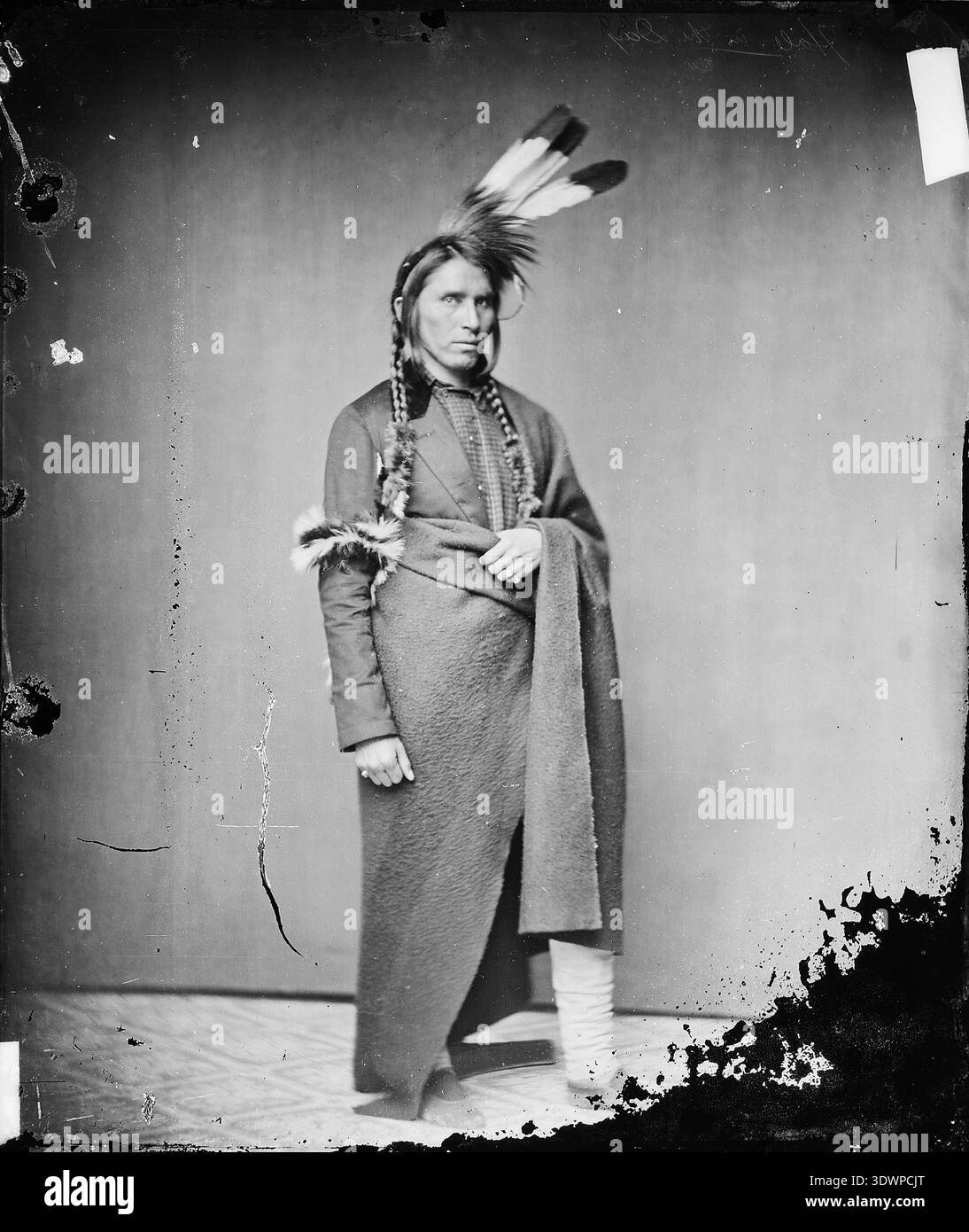 Dieses beeindruckende Porträt von Mathew Brady um 1860 zeigt Hole-in-the-Day den Jüngeren, einen prominenten Anführer der Ojibwe (Chippewa). Er trägt einen traditionellen gefiederten Kopfschmuck, Zöpfe und eine Decke, die sowohl indigene Kleidung als auch eine maßgeschneiderte Jacke zeigt. Stockfoto