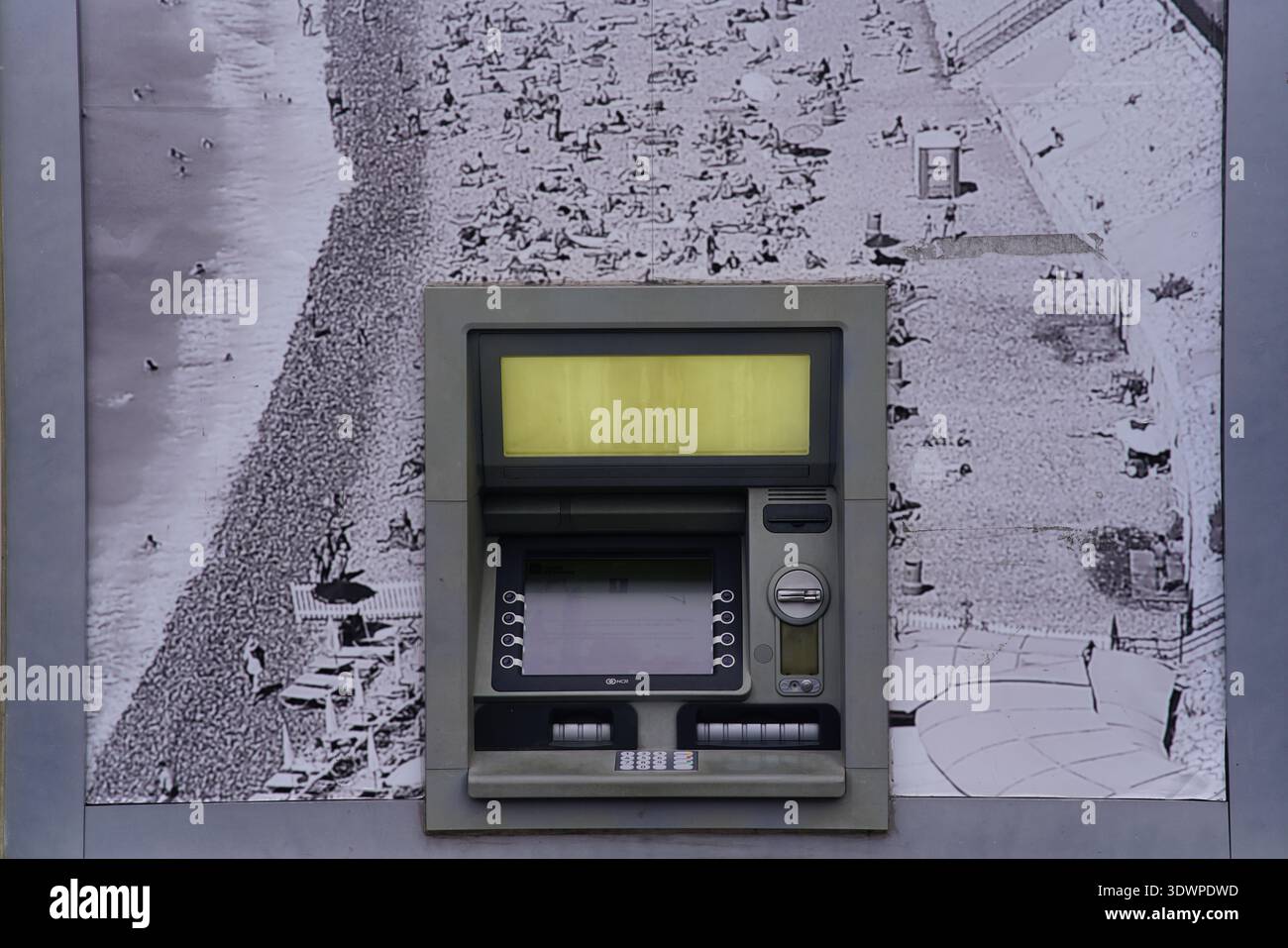 Vintage-Geldautomat vor einem großen schwarz-weißen Poster an einem überfüllten Strand in Nizza, Frankreich, für einen eindrucksvollen urbanen Kontrast. Stockfoto