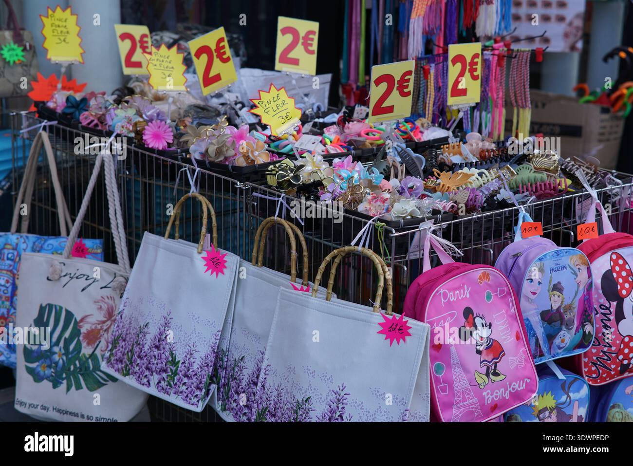 Der belebte Straßenmarkt ist voll mit bunten 2€ Haarschmuck, Blumenclips, Perlen Schmuck und lustigen bedruckten Einkaufstaschen und Kinderrucksack Stockfoto
