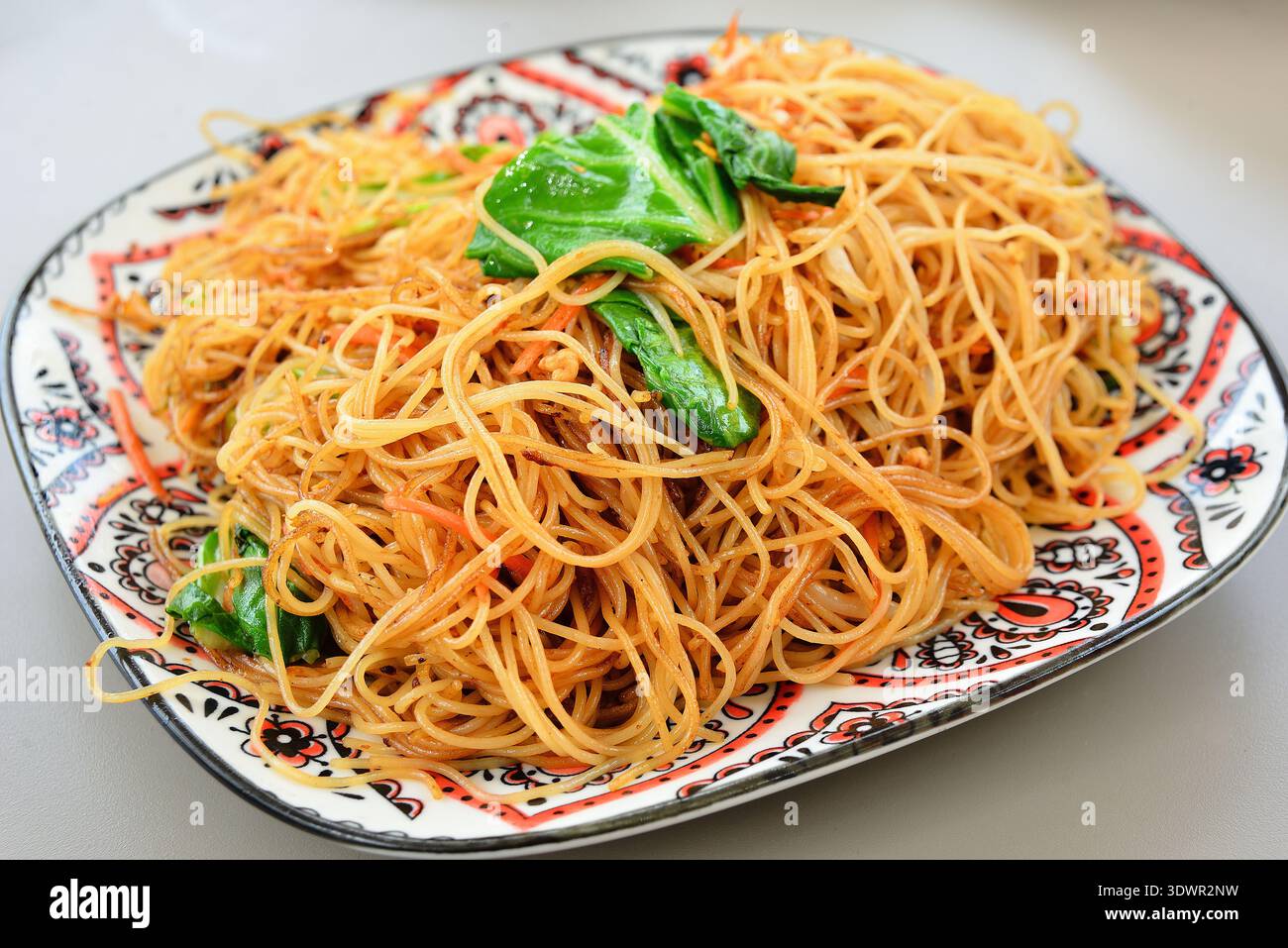 Ein Teller mit frittierten Reisnudeln auf dem Tisch. Es ist ein klassisches asiatisches Gericht, das in China, Thailand, Singapur, Malaysia, Vietnam, Indonesien usw. Stockfoto