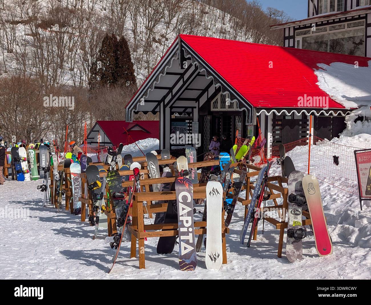Snowboards liegen auf Holzregalen vor der rot gedeckten Lodge in Hakuba Cortina, Japan Stockfoto