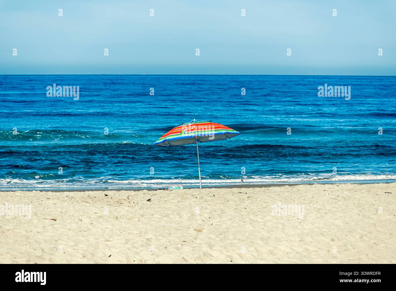 Einsamer farbenfroher Sonnenschirm am Strand. Stockfoto