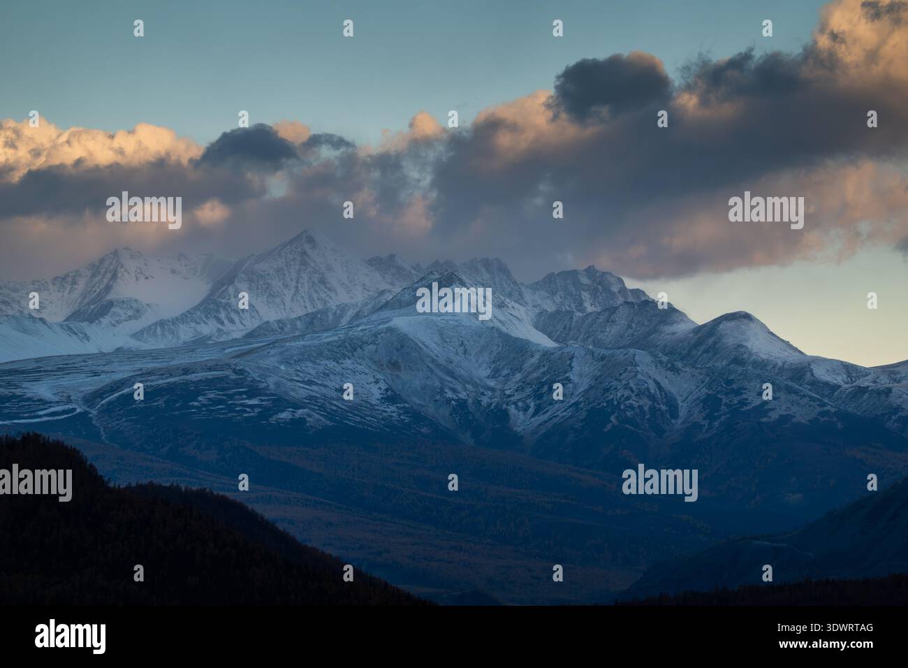 Schneebedeckte Berge bei Sonnenuntergang mit dramatischen Wolken, die eine malerische und ruhige Aussicht bieten. Stockfoto