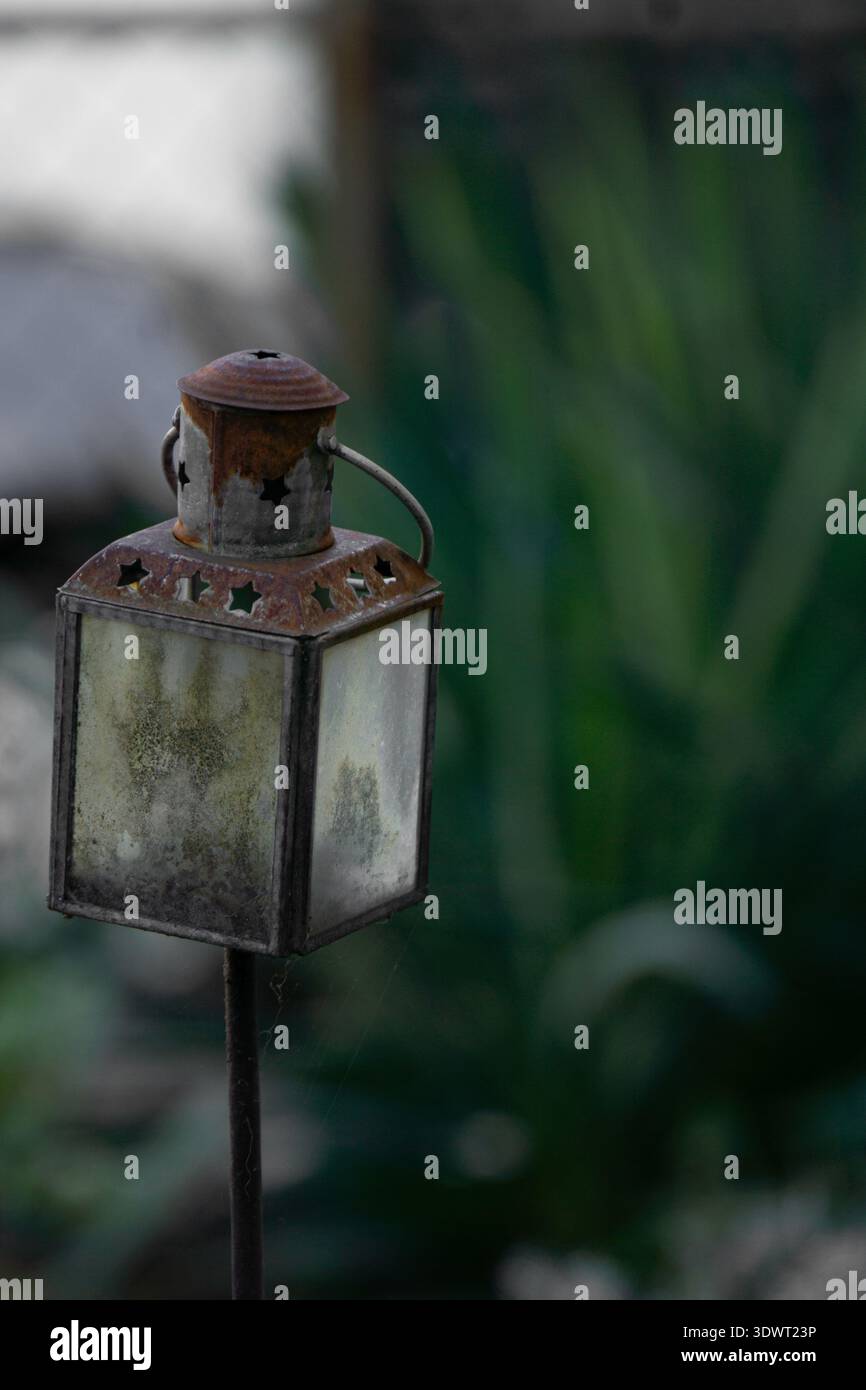 Rostige Vintage-Metalllaterne mit mattierten Glasplatten auf Gartenpfahl, auf weichem grünem Hintergrund mit geringer Schärfentiefe gestellt. Stockfoto