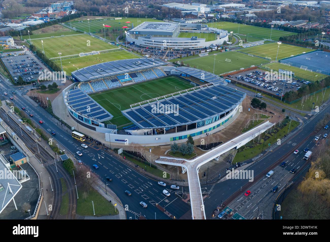 Luftbild des Etihad Campus in Manchester bei Sonnenuntergang mit dem Joie Stadium und der Fußgängerbrücke über den Alan Turing Way. Stockfoto