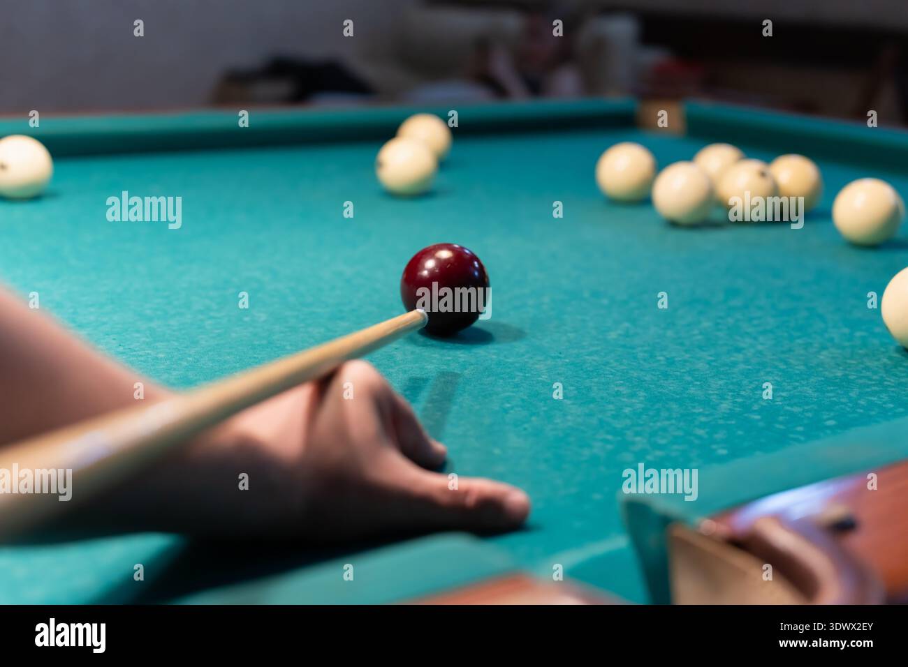 Männliche Hand, die Einen Cue-Stick auf den Roten Ball auf Einem grünen Billardtisch zielt. Stockfoto