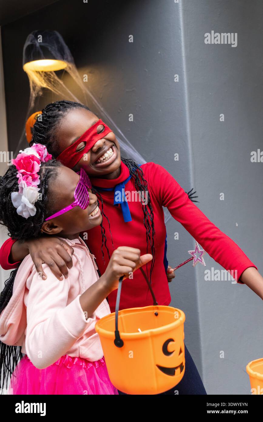 Afroamerikanische Kinder umarmen und lächeln beim Eintritt in das rote cape und halten Kürbiseimer in der Hand Stockfoto