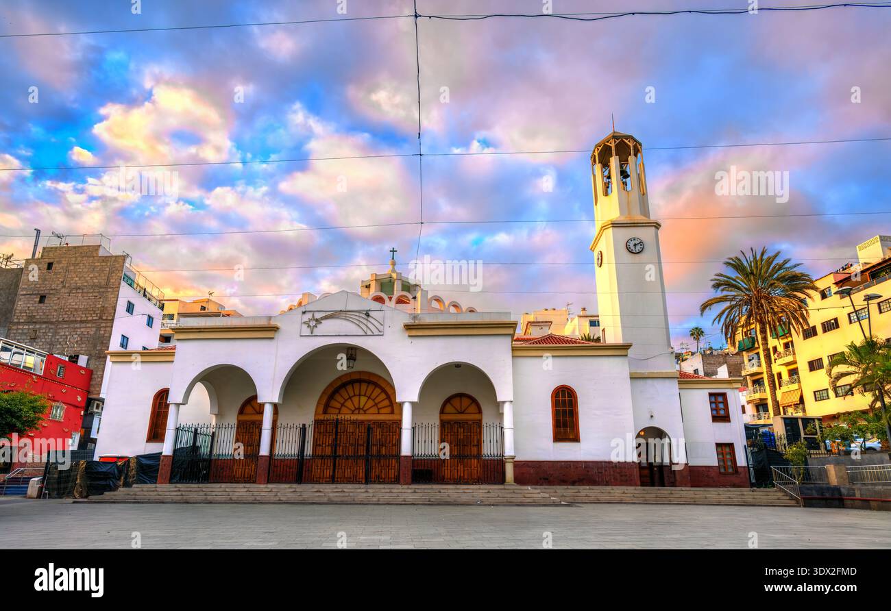 Malerischer Blick auf die weiße Fassade und den Glockenturm der Kirche Parroquia Nuestra Senora del Carmen unter einem farbenfrohen Himmel in Los Cristianos, Teneriffa. Stockfoto