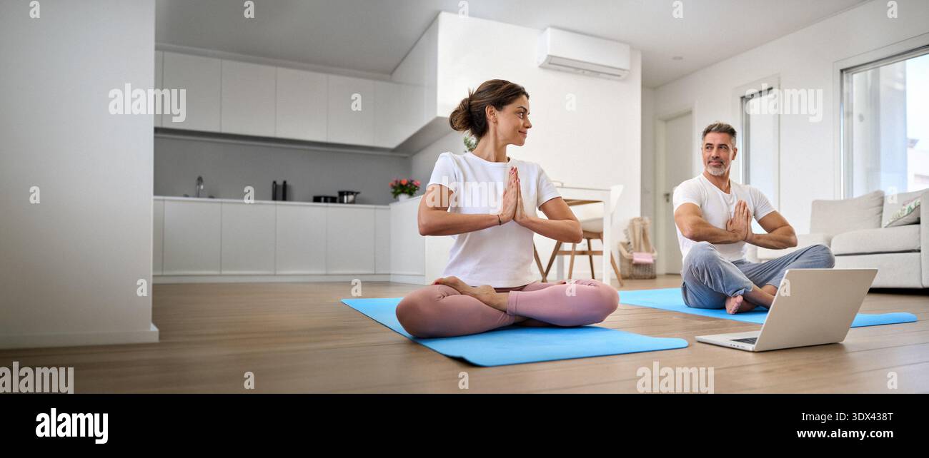 Ruhiges Paar mittleren Alters, das Online-Yoga-Meditation mit Laptop zu Hause lernt. Stockfoto