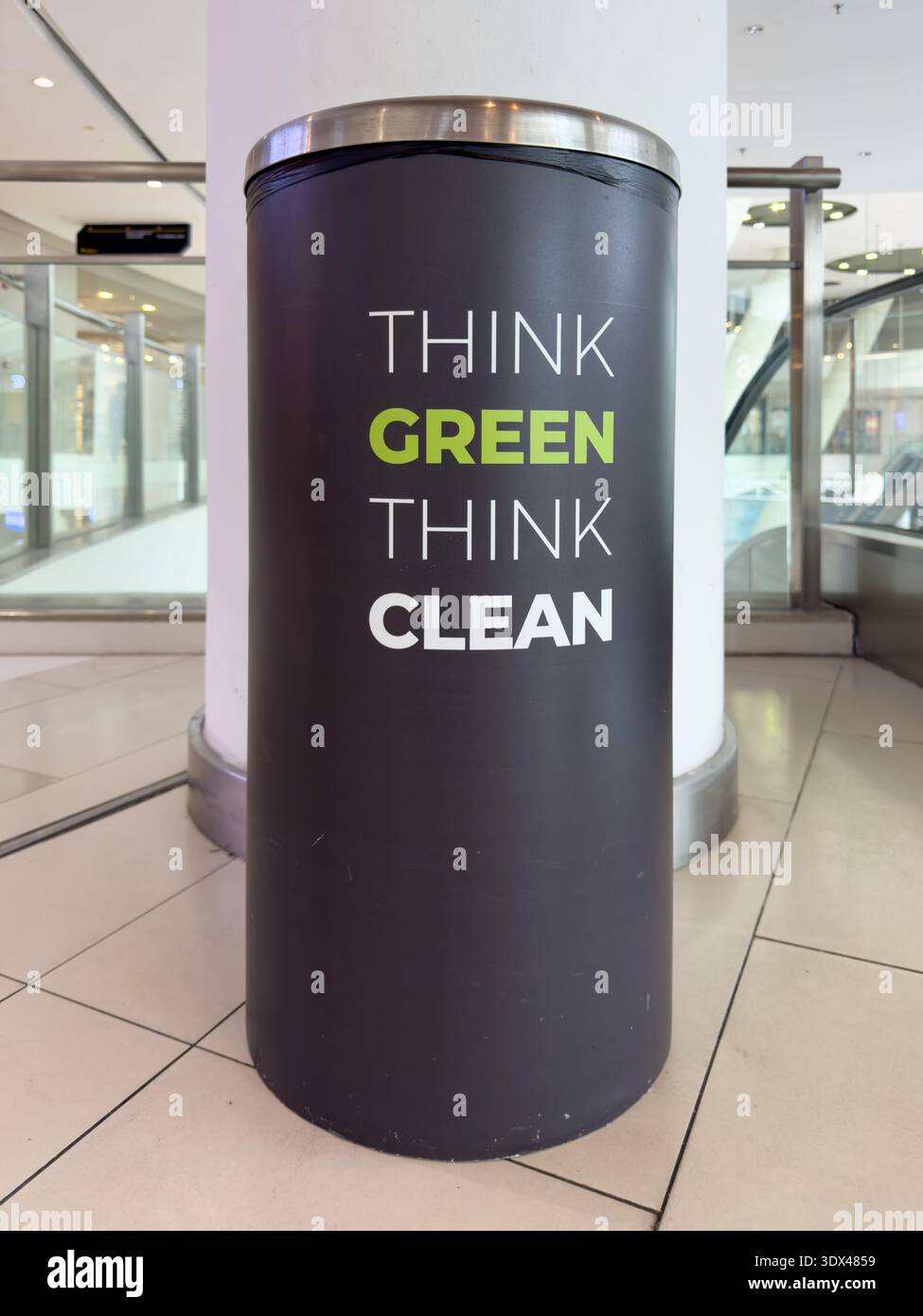 Penang, Malaysia - 18. Juni 2025: Runder Abfalleimer mit der Botschaft „Think Green Think Clean“ in einem modernen Einkaufszentrum mit sichtbaren Rolltreppen Stockfoto