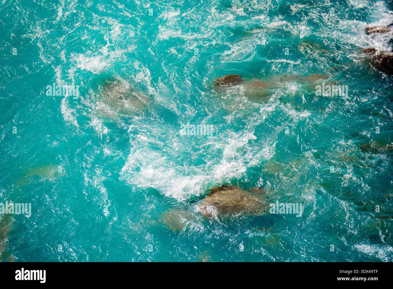 Gekräuseltes kristallklares, türkisfarbenes Flusswasser, das über glatte Steine und Kieselsteine in der Schlucht fließt Stockfoto