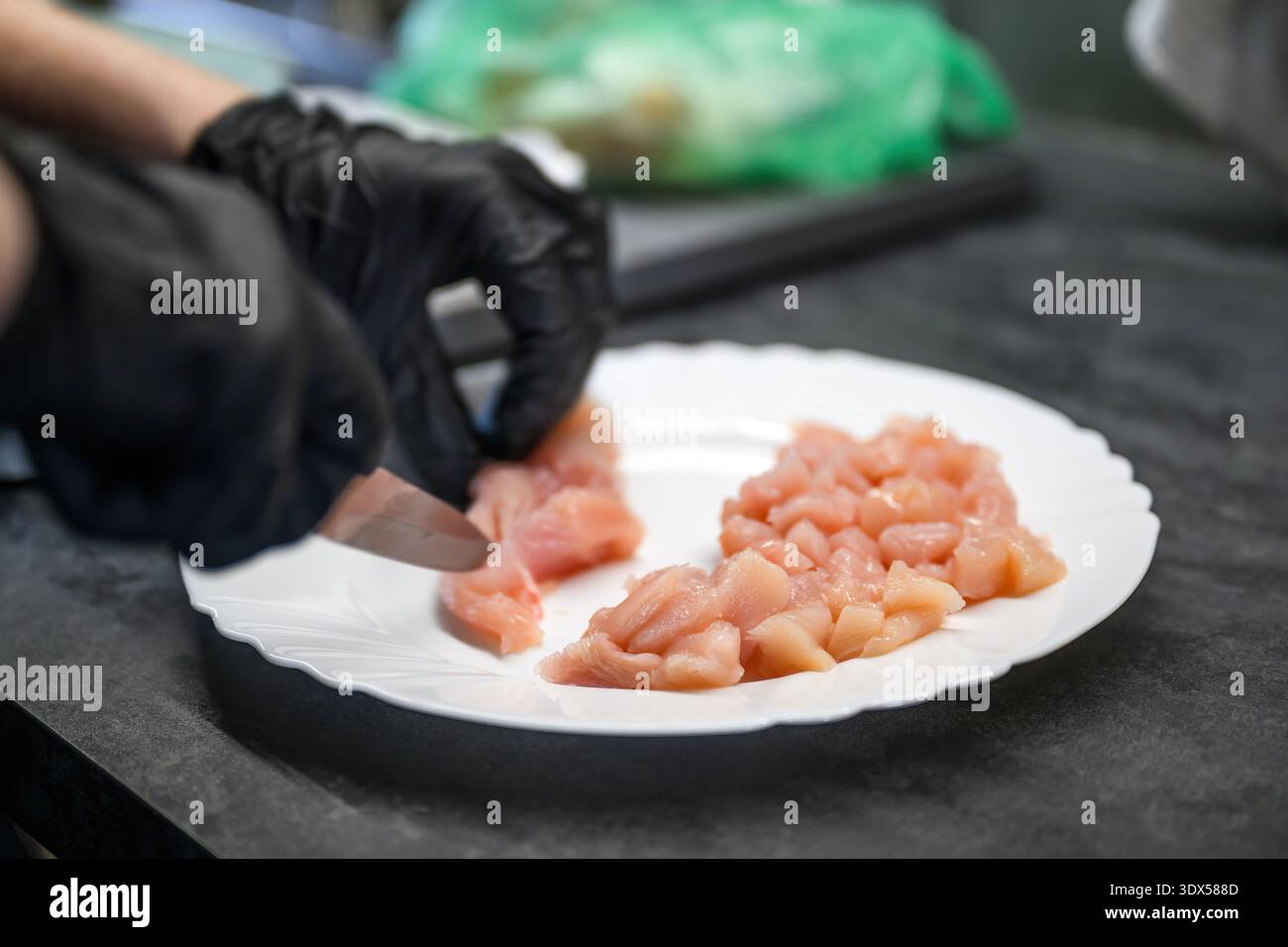 Nahaufnahme von weiblichen Handschuhen, die Geflügelfleisch auf der Küchenoberfläche schneiden. Konzept für die Handhabung von sauberen Lebensmitteln, in dem Zubereitung, Sicherheit und kulinarische Aspekte hervorgehoben werden Stockfoto