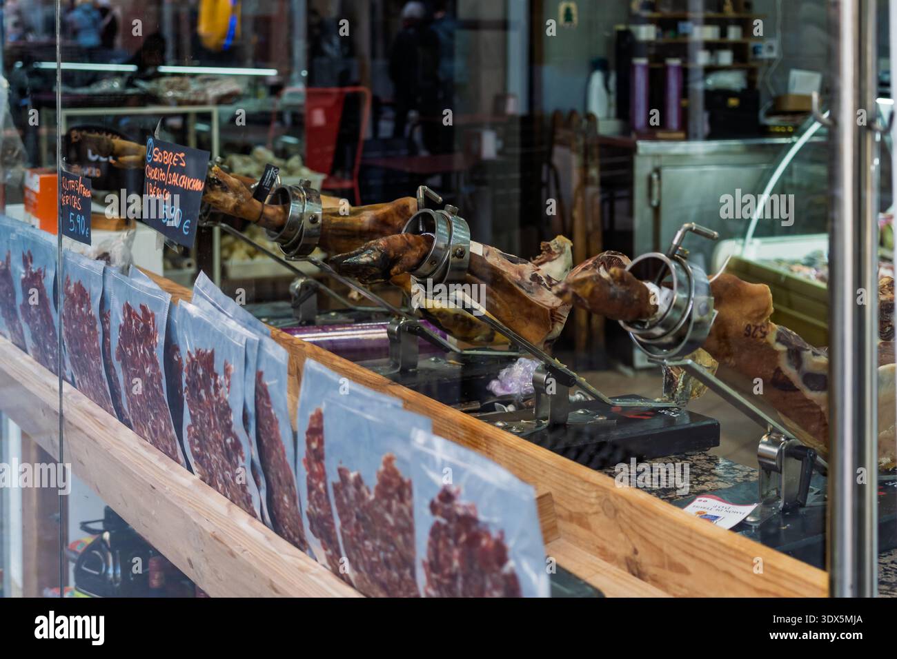 Barcelona, Spanien - 3. Februar 2026: Ausstellung von getrockneten iberischen Schinkenbeinen auf Haltern in einem Delikatessenfenster, das den traditionellen spanischen gastronom repräsentiert Stockfoto