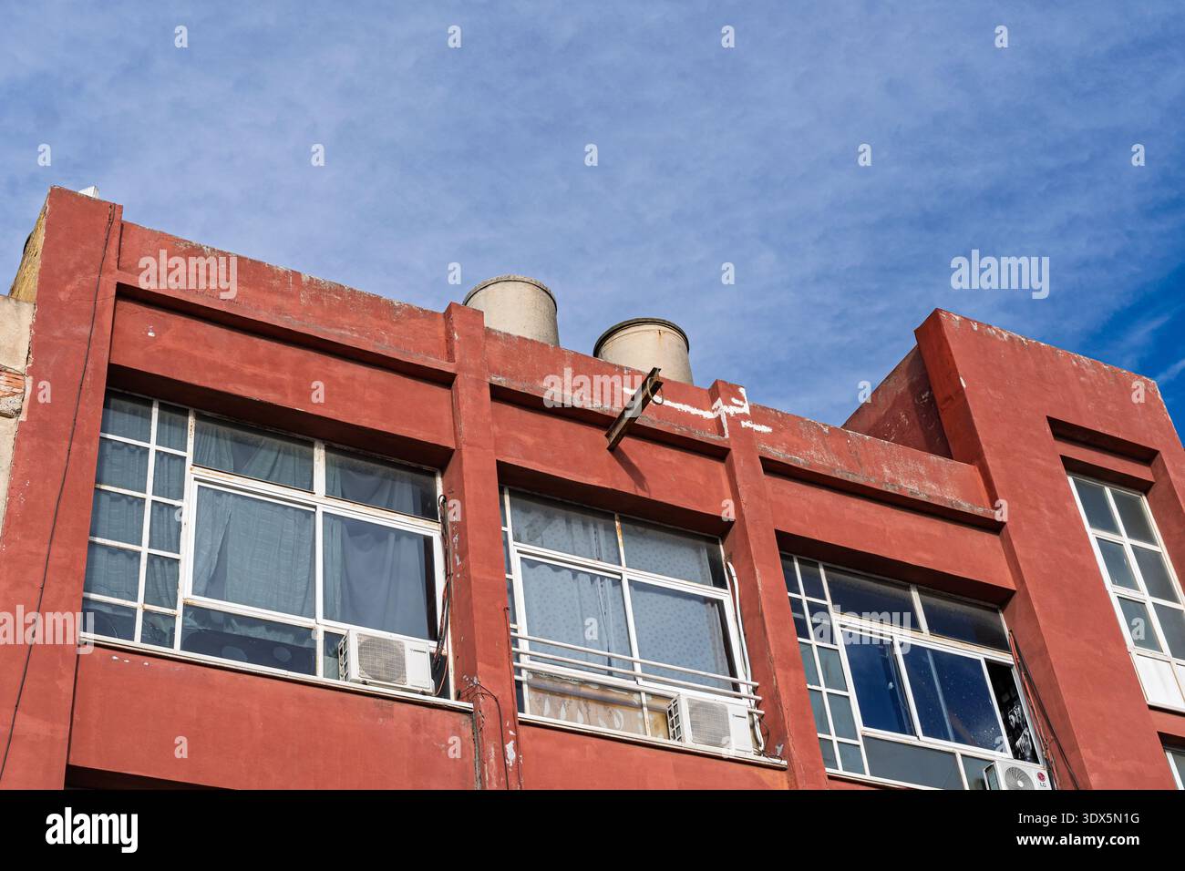 Badalona, Spanien - 3. Februar 2026: Fassade eines roten Wohngebäudes mit großen Fenstern mit weißen Rahmen und Klimaanlage Stockfoto
