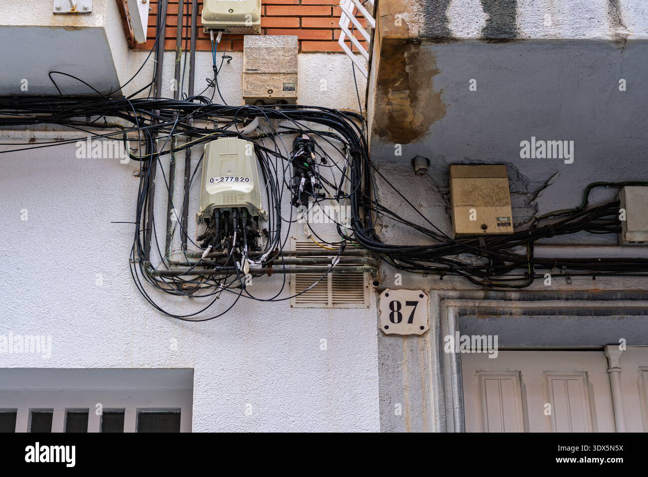 Badalona, Spanien - 3. Februar 2026: Unordentliches Bündel von Glasfaser- und Telefonleitungen, verbunden mit Abzweigdosen an einer Außenwand neben dem Haus Numb Stockfoto