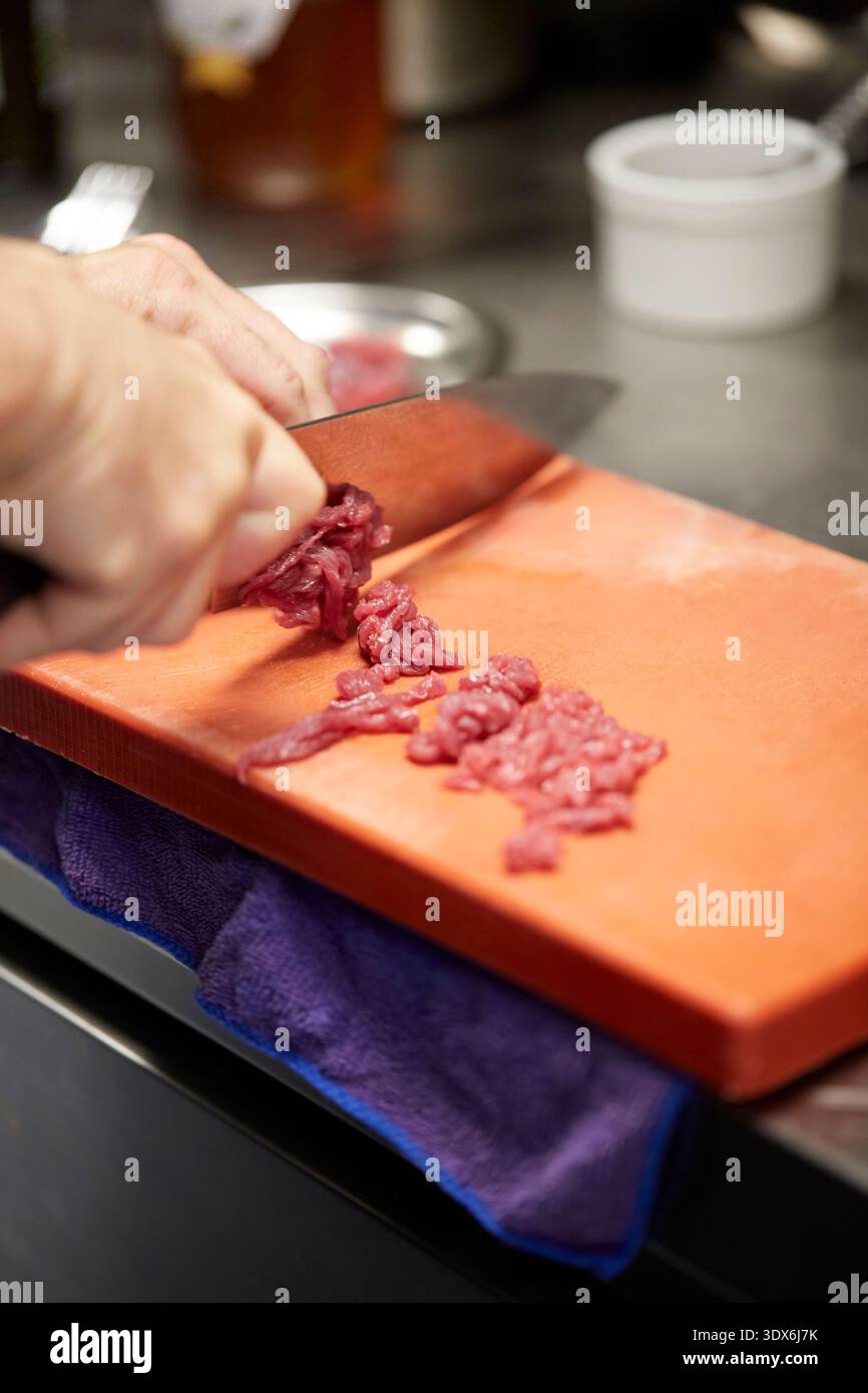 Ein Koch schneidet gekonnt rohes Fleisch auf einem sauberen Schneidebrett in einem Gourmet-Restaurant Küche. Die Liebe zum Detail unterstreicht die Präzision, die in benötigt wird Stockfoto