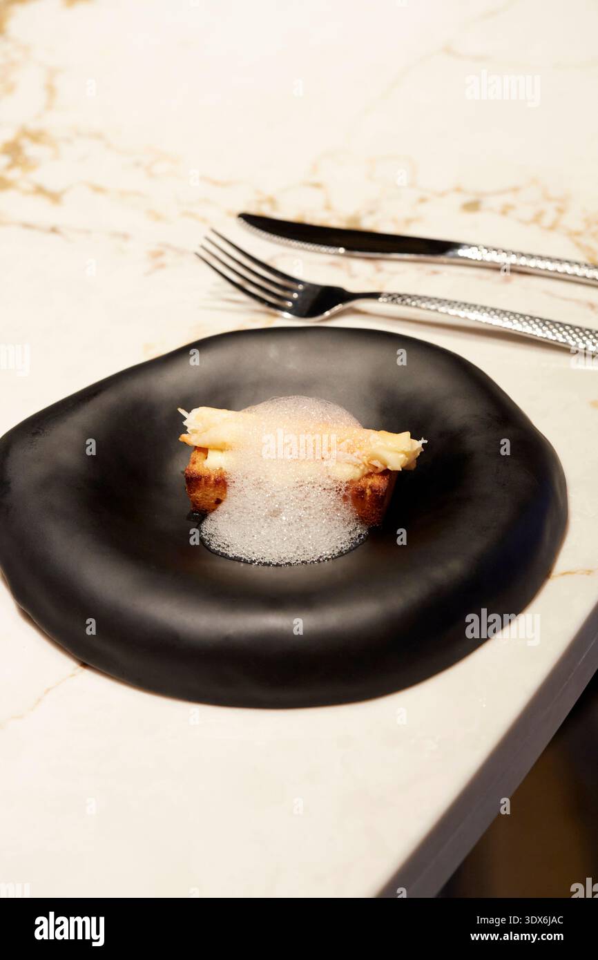 Ein Gourmet-Gericht mit modernem Schaum auf saftigem Fleisch, elegant serviert auf einem eleganten schwarzen Teller, perfekt für High-End-Res Stockfoto