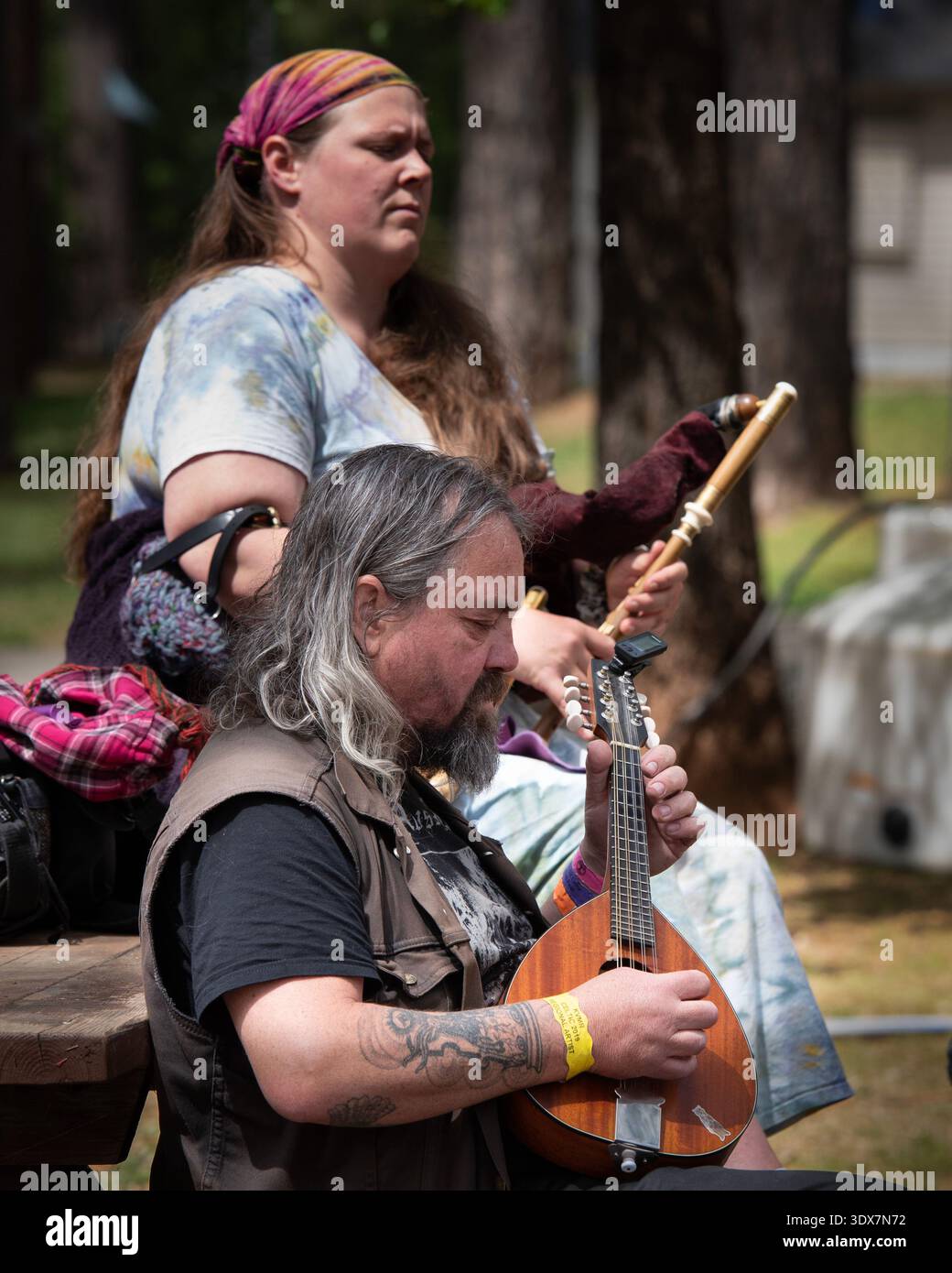 Grass Valley, 3. Mai 2025. Zwei Musiker treten beim Celtic Festival im Grass Valley auf. Man spielt ein Saiteninstrument, während man auf einem hölzernen ben sitzt Stockfoto