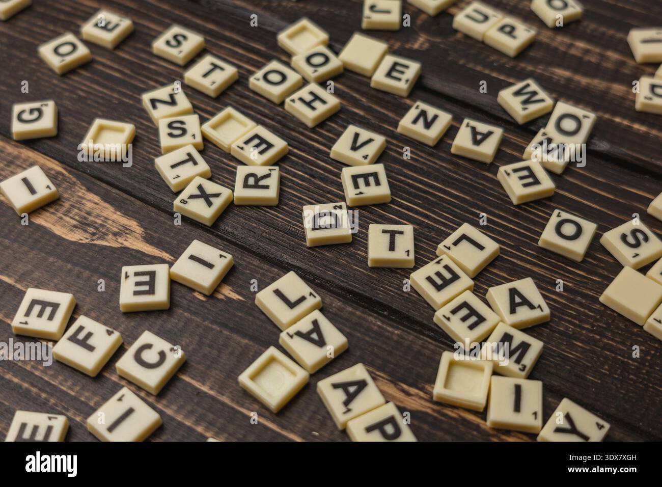Scrabble Fliesen sind auf einem Holztisch zum National Scrabble Day verstreut. Freunde treffen sich, um ein lustiges Wortspiel zu genießen und eac herauszufordern Stockfoto