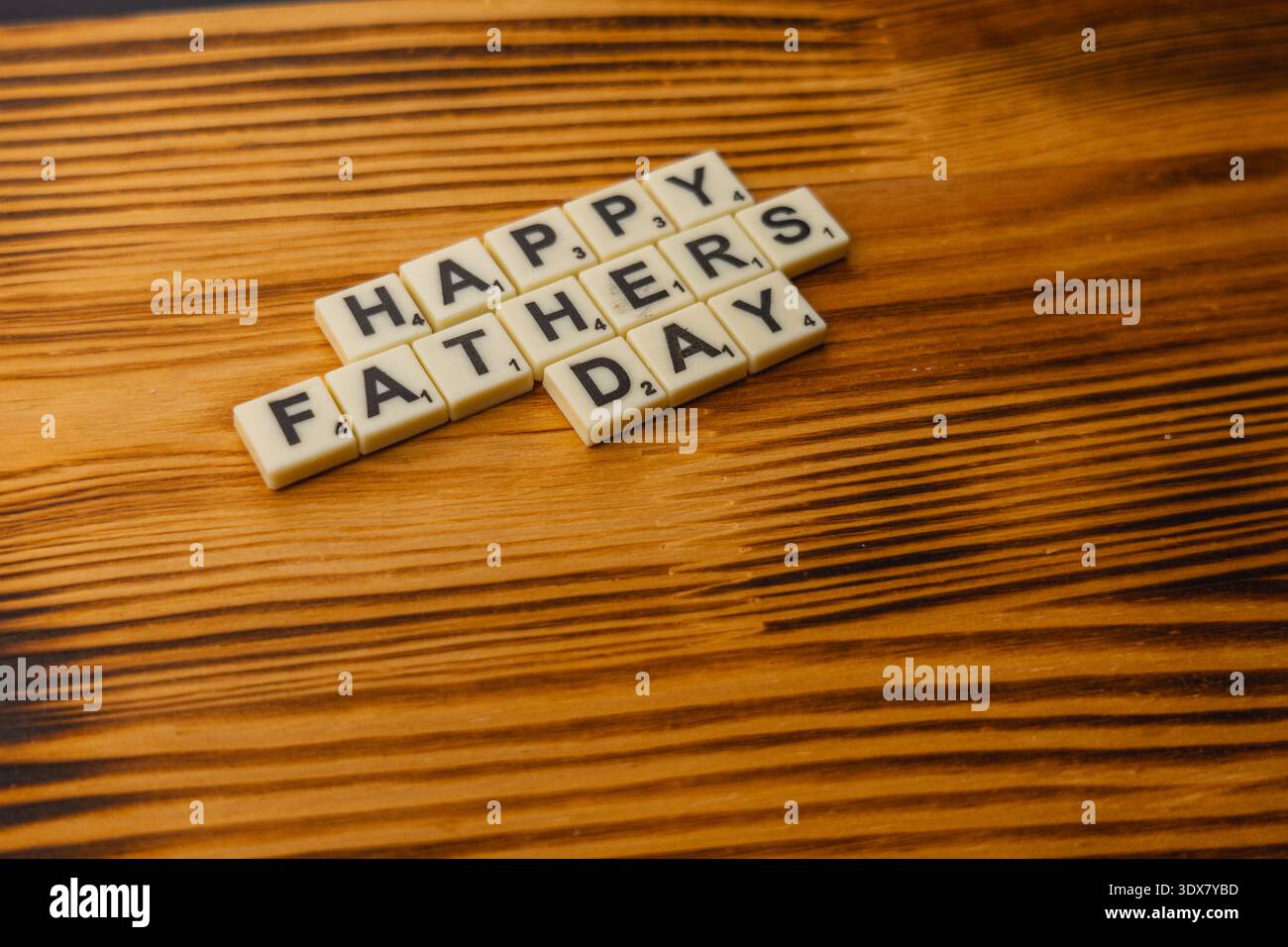 Die Leute versammeln sich um einen Holztisch, um Scrabble am National Scrabble Day zu spielen. Sie platzieren Buchstabensteine, um Nachrichten zu buchstabieren und genießen das Spiel gemeinsam. Stockfoto