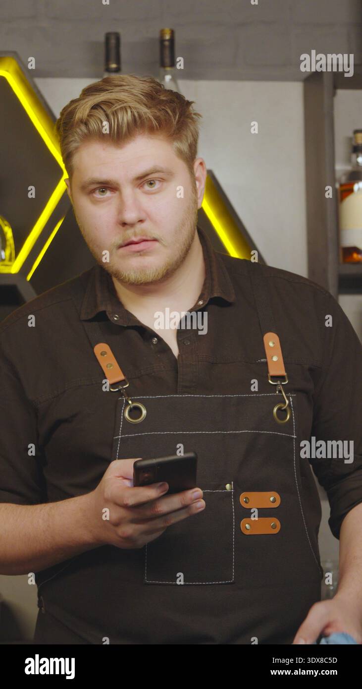 Barkeeper, der auf das Smartphone schaut, während er hinter der Bar arbeitet Stockfoto
