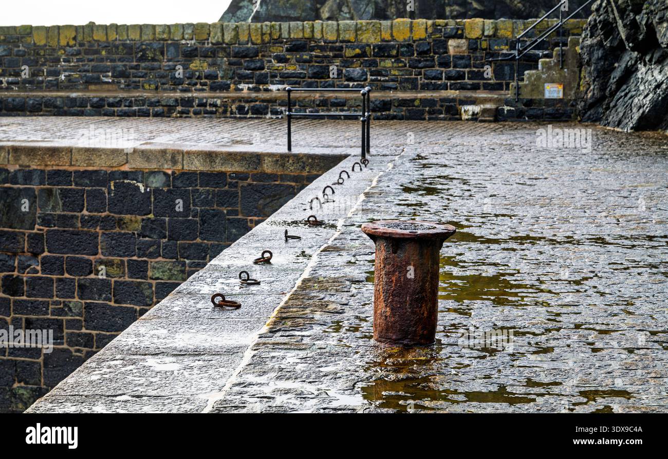 Rostiger Schiffspoller am Pier in der Meeresmauer am Hafen von Mullion Cove, Cornwall, England, Großbritannien. Stockfoto