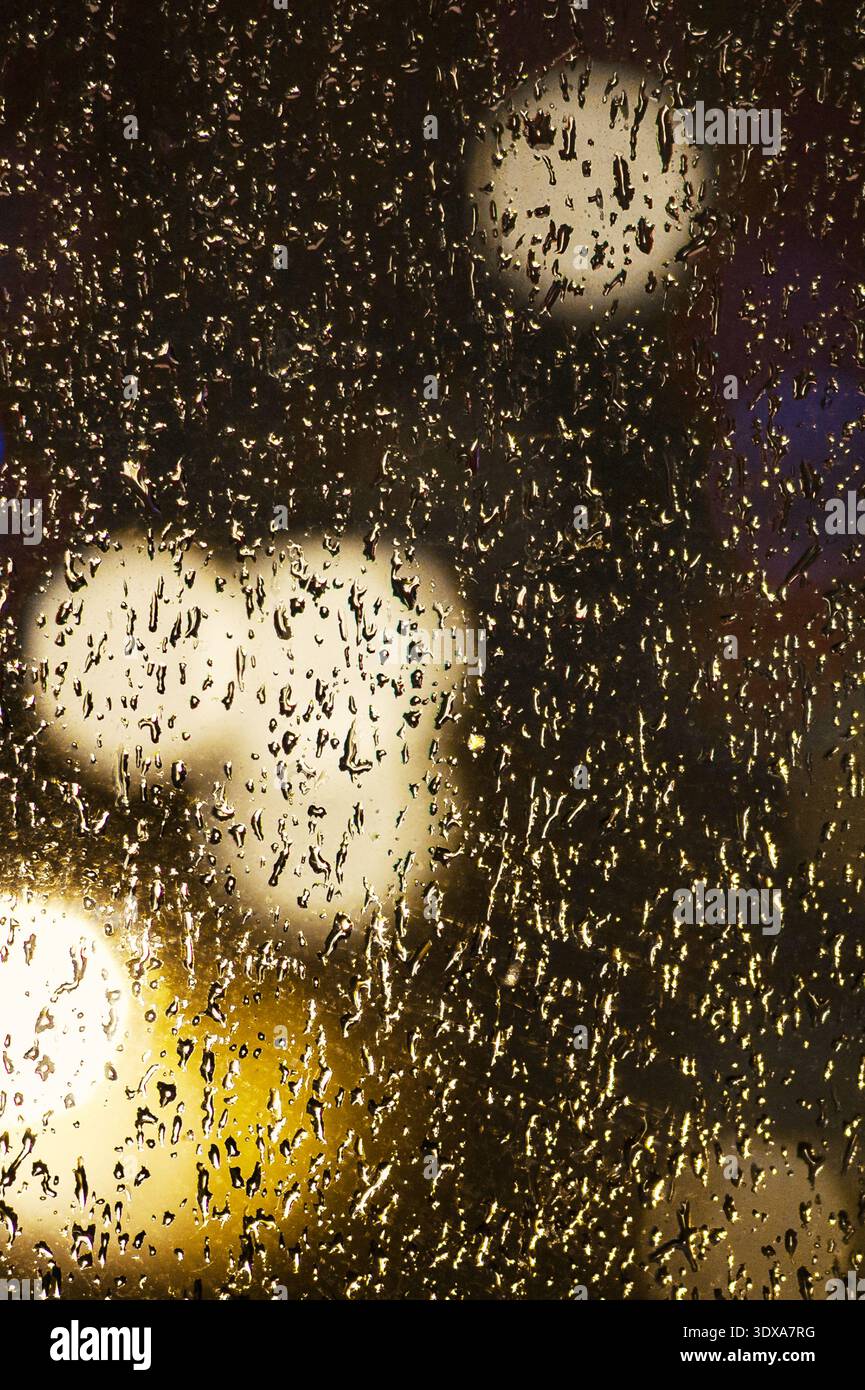 Tropfen auf Glas. Regentropfen an einem Fenster vor dem Hintergrund der Lichter der Stadt bei Nacht. Regentropfen in einem Fensterbereich Stockfoto