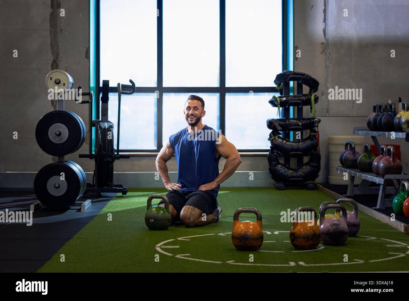 Lächelnder Mann mit Armen akimbo kniend auf dem Boden während des Trainings im Fitnessstudio Stockfoto