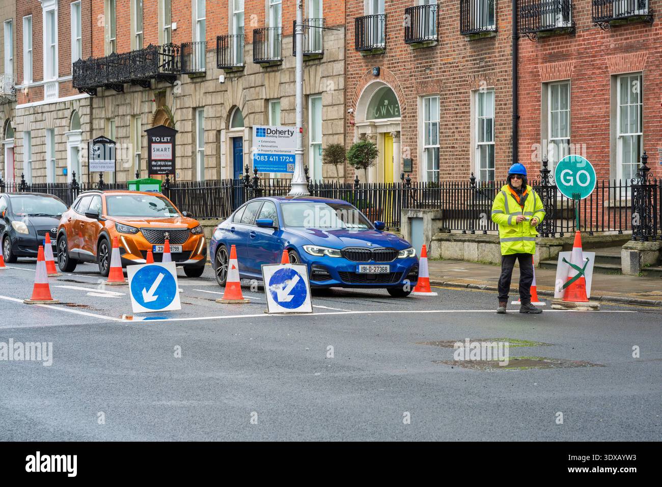 Der Verkehr fließt durch Baustellen am Merrion Square, Dublin, mit gut sichtbaren Arbeitern und georgianischen Stadthäusern Stockfoto