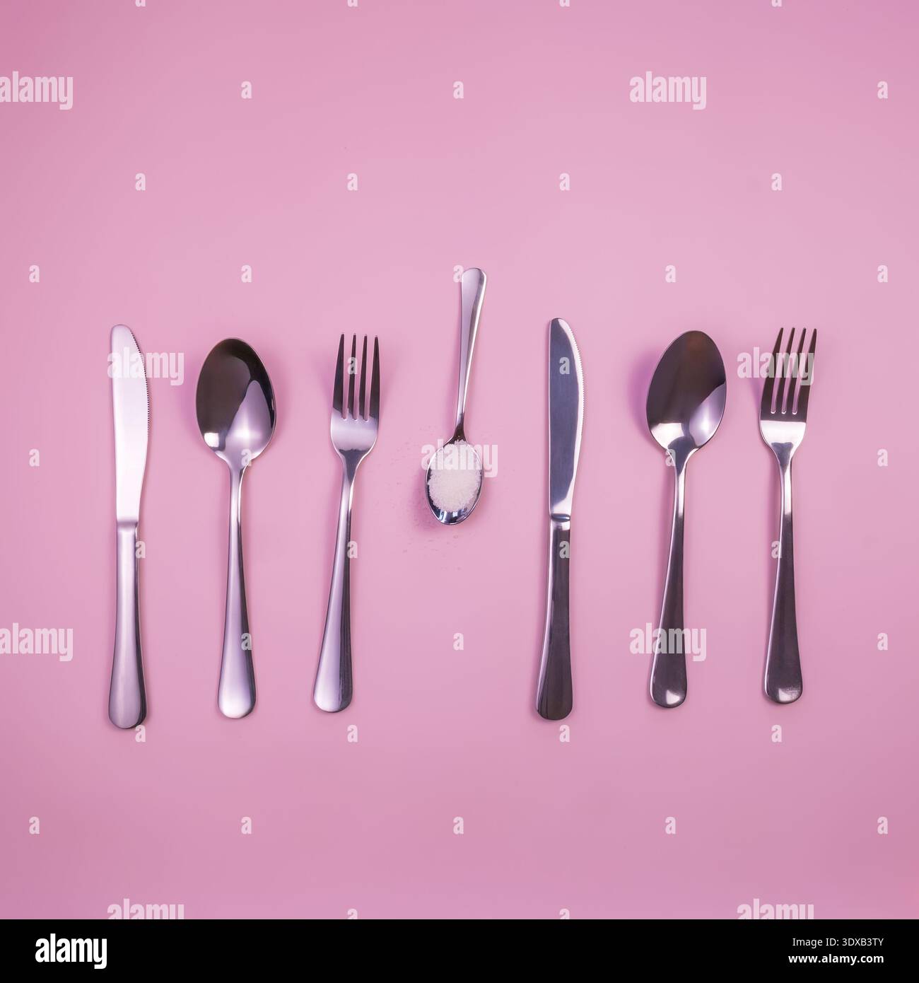 Eine Kollektion von Edelstahlbesteck auf rosa Hintergrund. Umfasst Messer, Gabeln und Löffel in verschiedenen Größen und Formen. Stockfoto