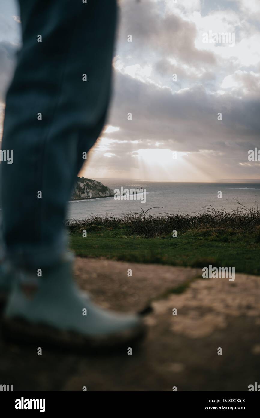 Eine Person steht am Strand mit Blick auf das Meer. Der Himmel ist bewölkt und die Sonne scheint durch die Wolken Stockfoto